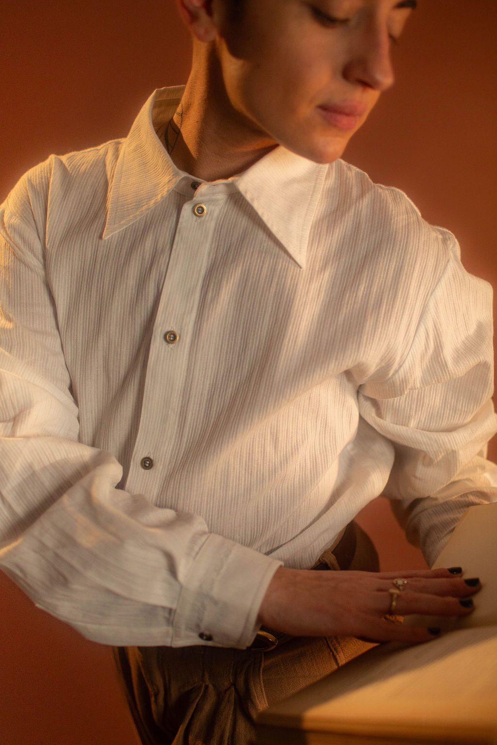 White cotton button up with a tone on tone stripe. Featuring wooden buttons and embroidered latin phrase on the back and cuffs translates to 'finding yourself in the whispers of the world'.