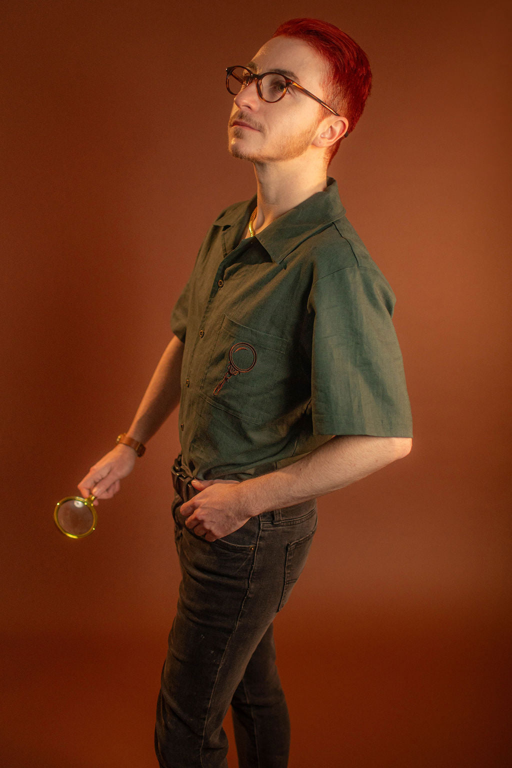 Crisp moss green camp shirt with a linen and cotton blend. With brass brown buttons and a bronze magnifying glass embroidered on the front pocket.