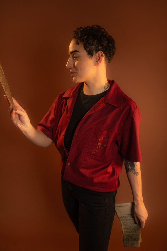 Crisp wine red camp shirt with a linen and cotton blend. With brass brown buttons and a bronze magnifying glass embroidered on the front pocket.