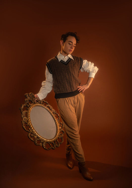 Brown and black wool and nylon blend tweed sweater vest with tennis sweater style black and off-white striped collar and sleeve cuffs. A small, black embroidered magnifying glass on front chest. Featured with our Classics White Button up.