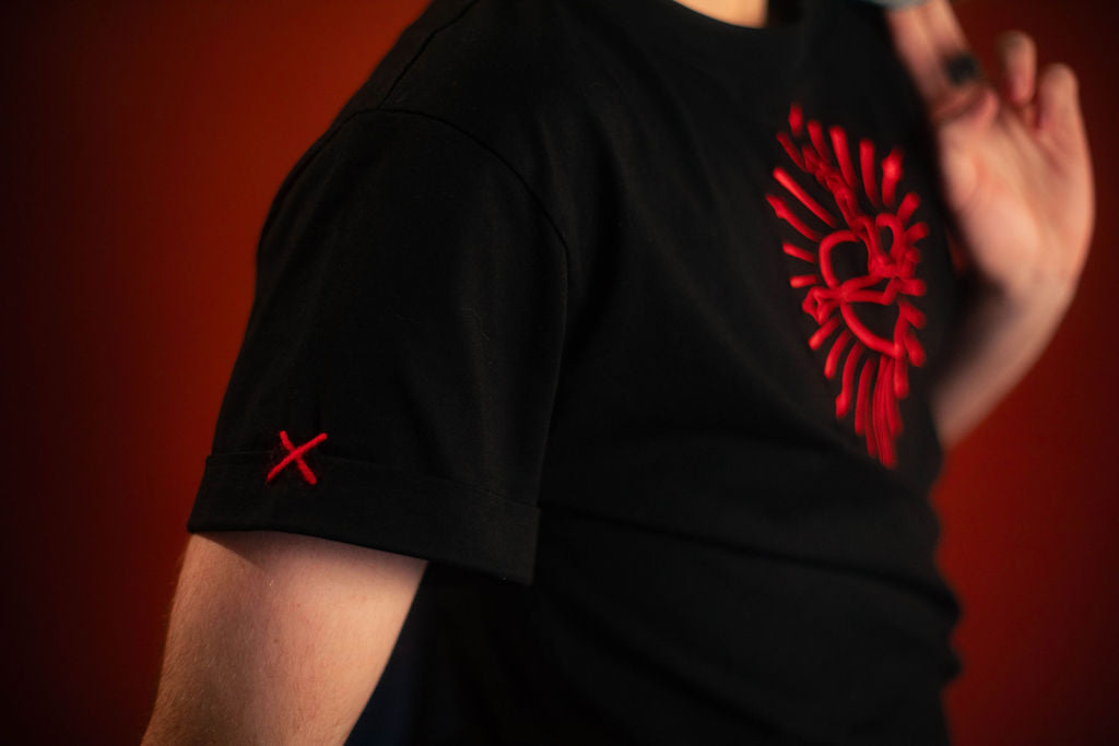 Black 100% cotton tshirt with embroidered red sword and heart design on chest, cuffed sleeves with a hand-tacked red X on one, printed collar information, and Saints & Sonnets heart and sword logo on a red hem tag and printed in red on the back collar.