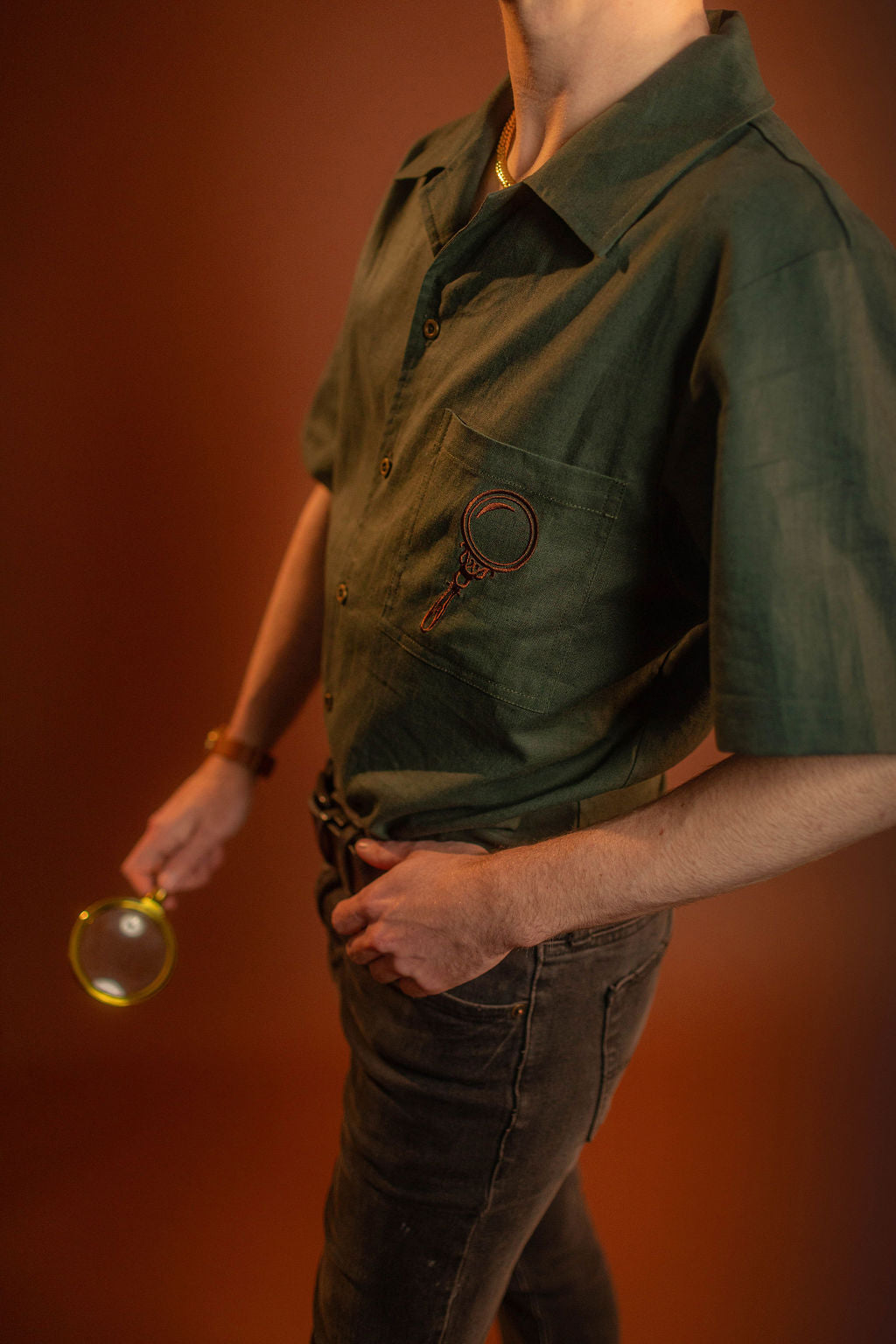 Crisp moss green camp shirt with a linen and cotton blend. With brass brown buttons and a bronze magnifying glass embroidered on the front pocket.