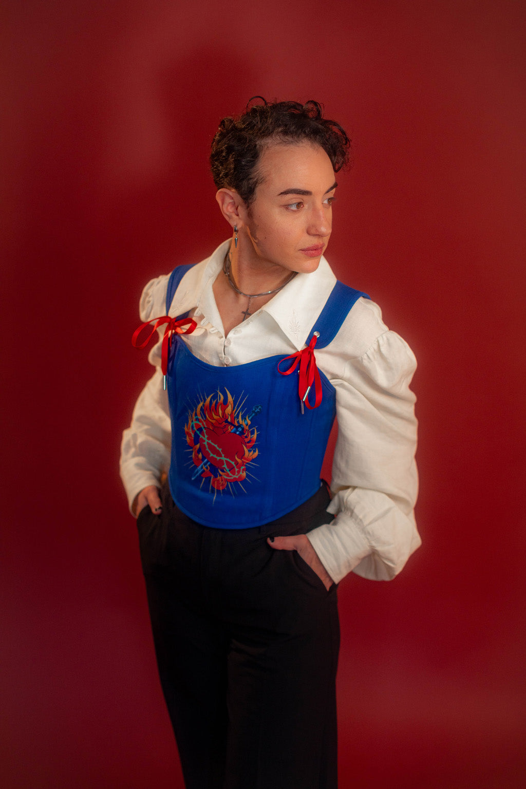 Reversible corset top with floral brocade matching our Montague button up and Lovers Favor bandana on one side and a cobalt blue cotton twill on the other with a printed red, orange, yellow, teal, and silver sacred heart in the middle. Nylon boning for shape, red and blue pairs of satin ribbon to tie removable straps and lace up the back. Featured with our Starcrossed Poet Shirt.