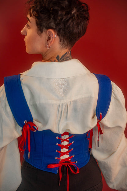 Reversible corset top with floral brocade matching our Montague button up and Lovers Favor bandana on one side and a cobalt blue cotton twill on the other with a printed red, orange, yellow, teal, and silver sacred heart in the middle. Nylon boning for shape, red and blue pairs of satin ribbon to tie removable straps and lace up the back. Featured with our Starcrossed Poet Shirt.