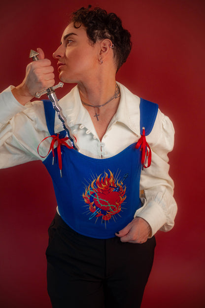 Reversible corset top with floral brocade matching our Montague button up and Lovers Favor bandana on one side and a cobalt blue cotton twill on the other with a printed red, orange, yellow, teal, and silver sacred heart in the middle. Nylon boning for shape, red and blue pairs of satin ribbon to tie removable straps and lace up the back. Featured with our Starcrossed Poet Shirt.