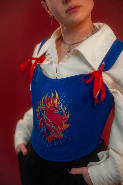 Reversible corset top with floral brocade matching our Montague button up and Lovers Favor bandana on one side and a cobalt blue cotton twill on the other with a printed red, orange, yellow, teal, and silver sacred heart in the middle. Nylon boning for shape, red and blue pairs of satin ribbon to tie removable straps and lace up the back. Featured with our Starcrossed Poet Shirt.