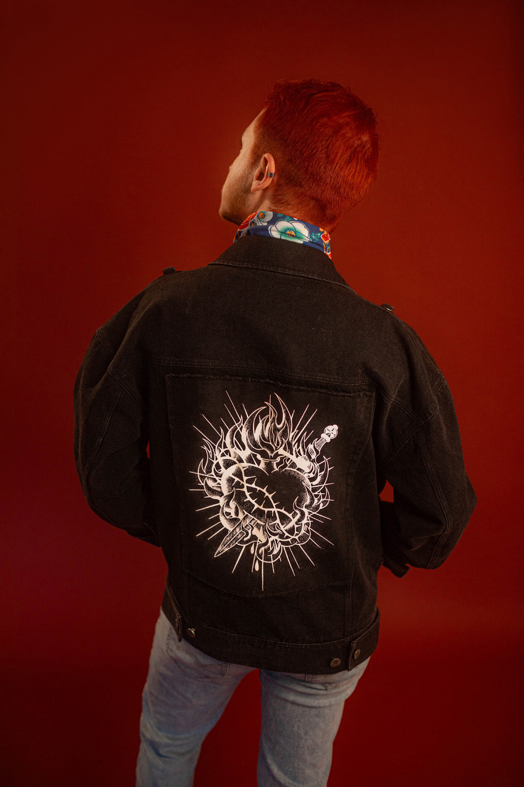 Black sturdy cotton denim jacket with white screen-printed sword on chest pocket and sacred heart graphic on a back patch. Custom pearl button on front pocket aligned with sword's pommel, five pockets, and multiple reinforced D rings for clipping accessories on to, like our Heart On Your Pocket Chain. Shown here with our Lovers Favor Bandana.