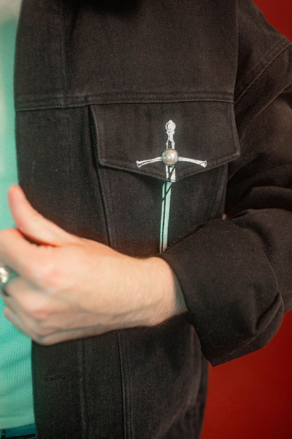 Black sturdy cotton denim jacket with white screen-printed sword on chest pocket and sacred heart graphic on a back patch. Custom pearl button on front pocket aligned with sword's pommel, five pockets, and multiple reinforced D rings for clipping accessories on to, like our Heart On Your Pocket Chain. Shown here with our Lovers Favor Bandana.