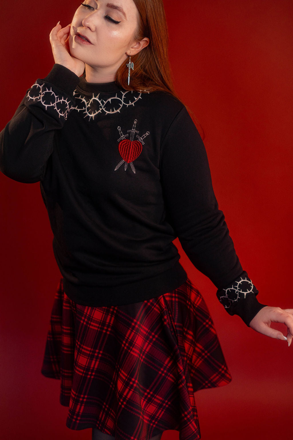 Soft 100% cotton fleece-lined black crewneck sweatshirt. Soft-backed embroidered silver thorn pattern around the collar and cuffs, silver and red three of swords embroidered on chest, with three swords crossed between a red heart.