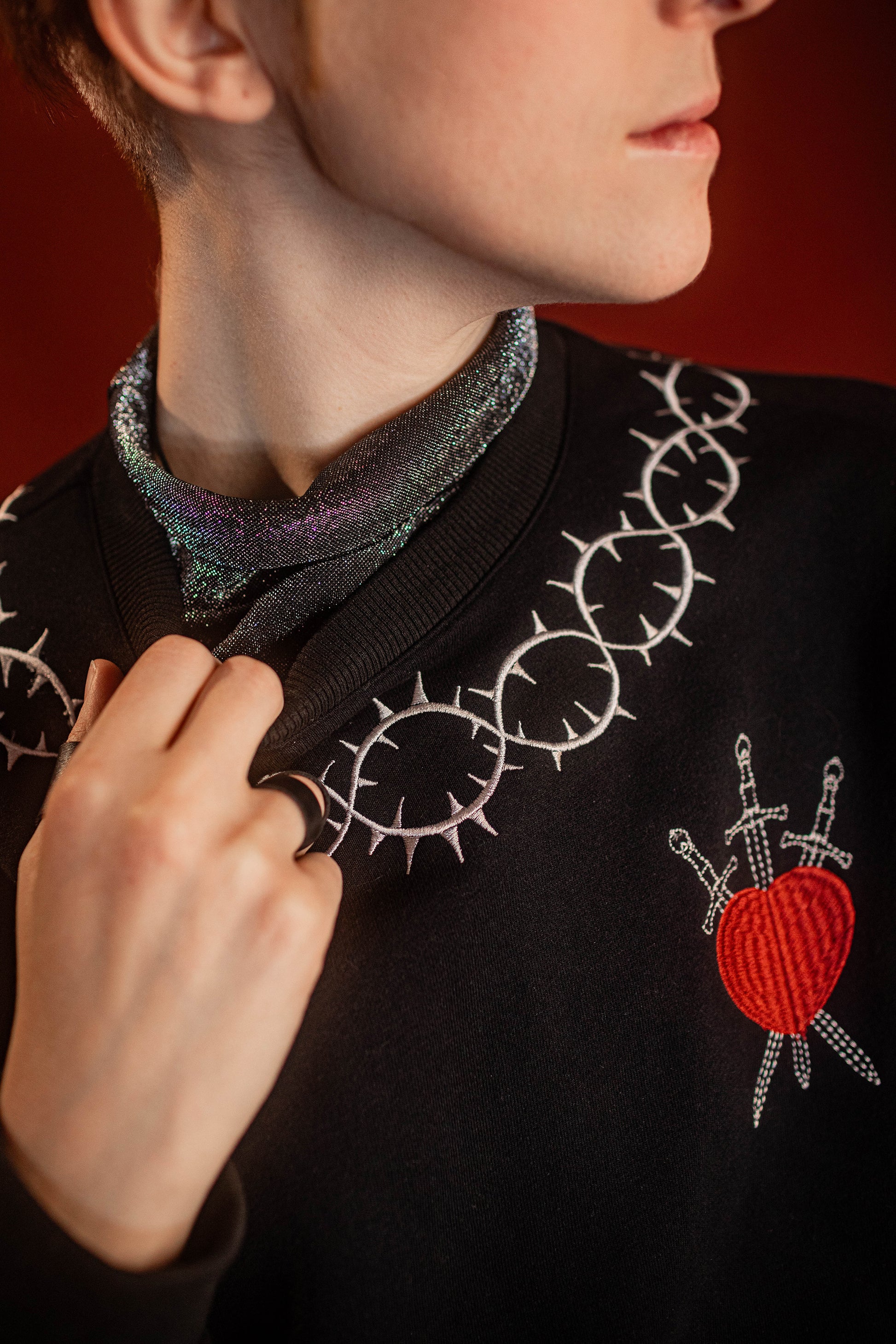 Soft 100% cotton fleece-lined black crewneck sweatshirt. Soft-backed embroidered silver thorn pattern around the collar and cuffs, silver and red three of swords embroidered on chest, with three swords crossed between a red heart. Featured here with our Chainmaille removable Collar dickie.