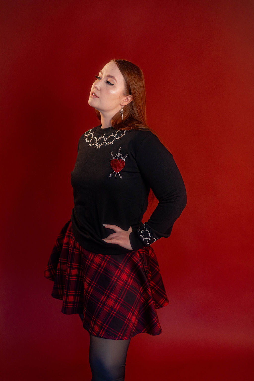 Soft 100% cotton fleece-lined black crewneck sweatshirt. Soft-backed embroidered silver thorn pattern around the collar and cuffs, silver and red three of swords embroidered on chest, with three swords crossed between a red heart.