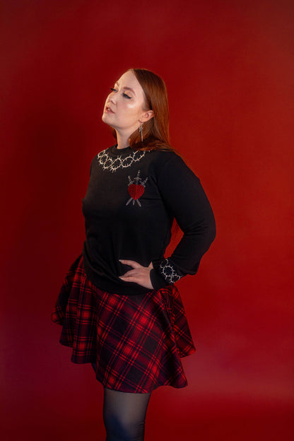 Soft 100% cotton fleece-lined black crewneck sweatshirt. Soft-backed embroidered silver thorn pattern around the collar and cuffs, silver and red three of swords embroidered on chest, with three swords crossed between a red heart.
