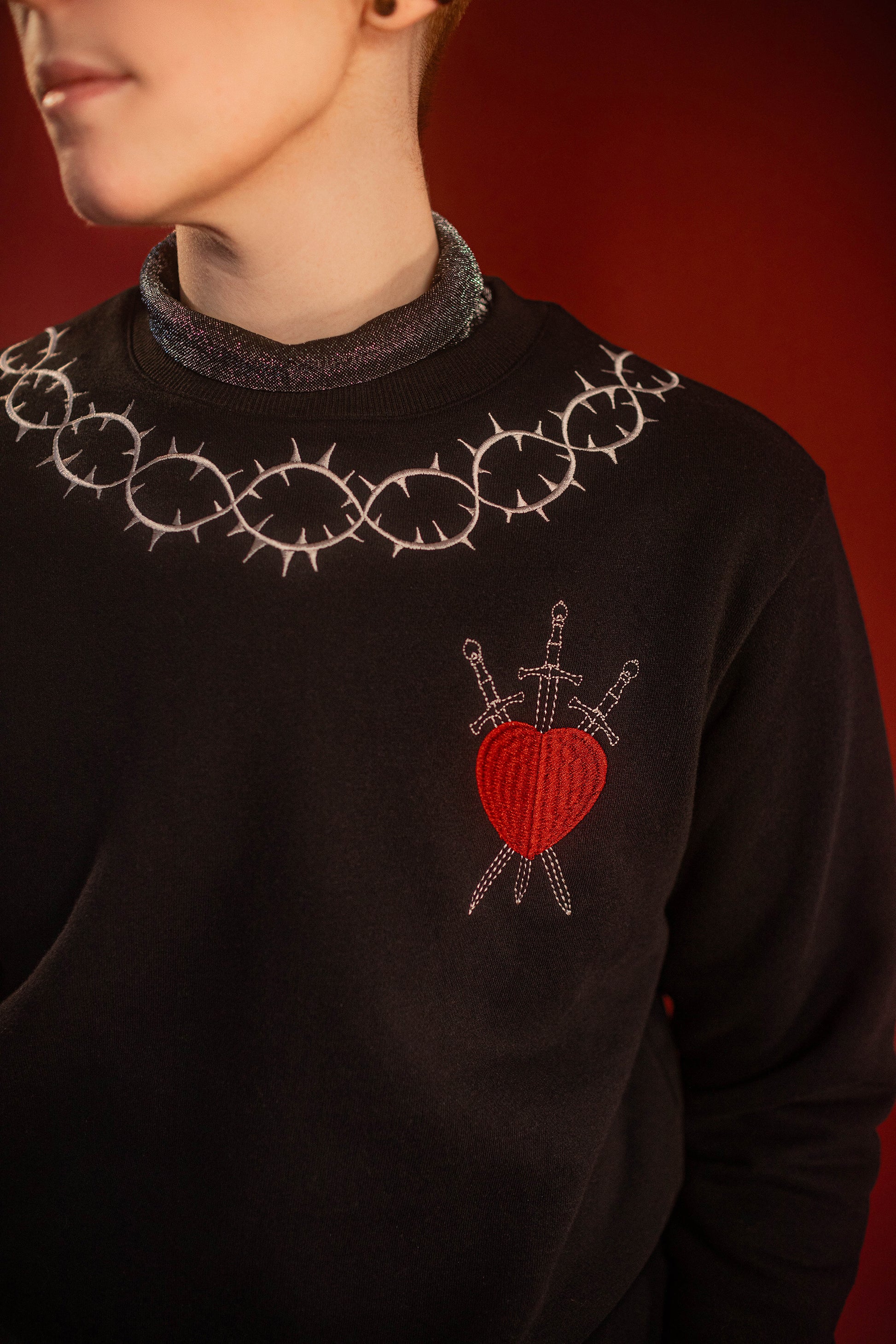 Soft 100% cotton fleece-lined black crewneck sweatshirt. Soft-backed embroidered silver thorn pattern around the collar and cuffs, silver and red three of swords embroidered on chest, with three swords crossed between a red heart. Featured here with our Chainmaille removable Collar dickie.