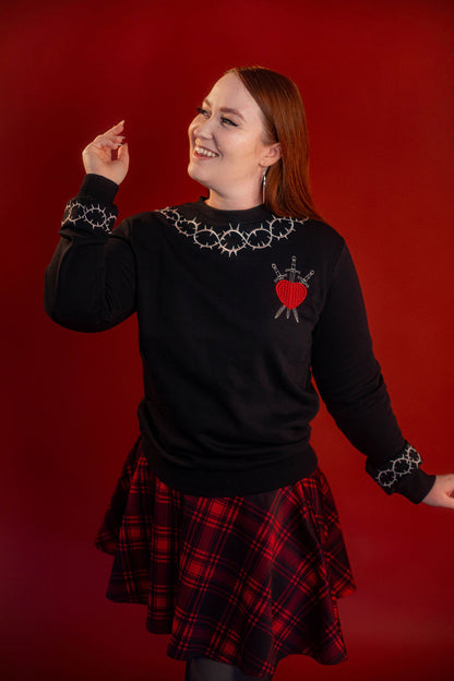 Soft 100% cotton fleece-lined black crewneck sweatshirt. Soft-backed embroidered silver thorn pattern around the collar and cuffs, silver and red three of swords embroidered on chest, with three swords crossed between a red heart.