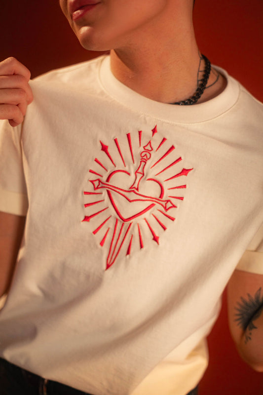 Off-white 100% cotton tshirt with embroidered red sword and heart design on chest, cuffed sleeves with a hand-tacked red X on one, printed collar information, and Saints & Sonnets heart and sword logo on a red hem tag and printed in red on the back collar.