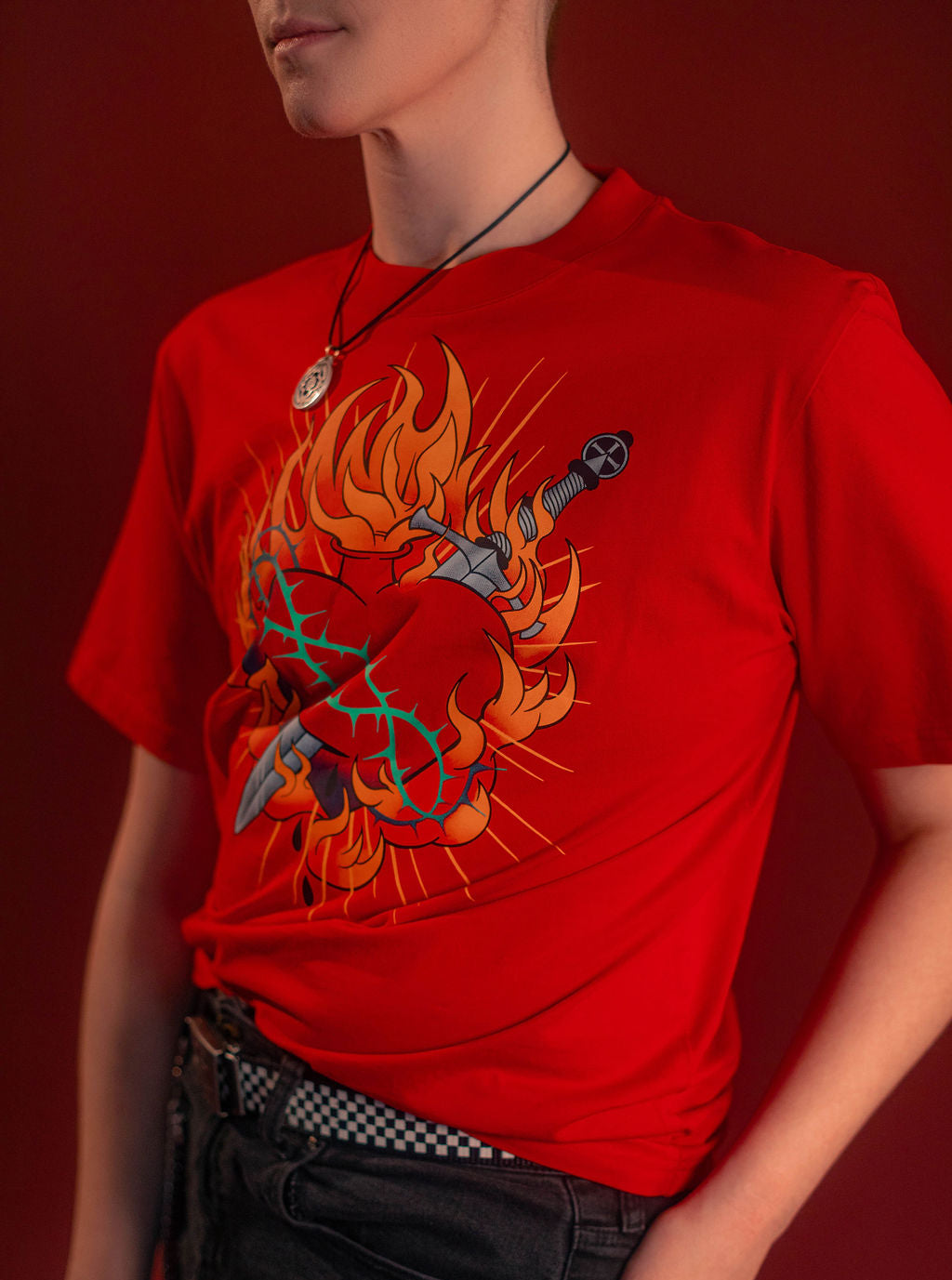 Fire red cotton tshirt with a full-color print on the front featuring the custom yellow, orange, teal, and silver flaming heart graphic with dagger and thorns. Printed collar tag information, and Saints & Sonnets logo hem tag.