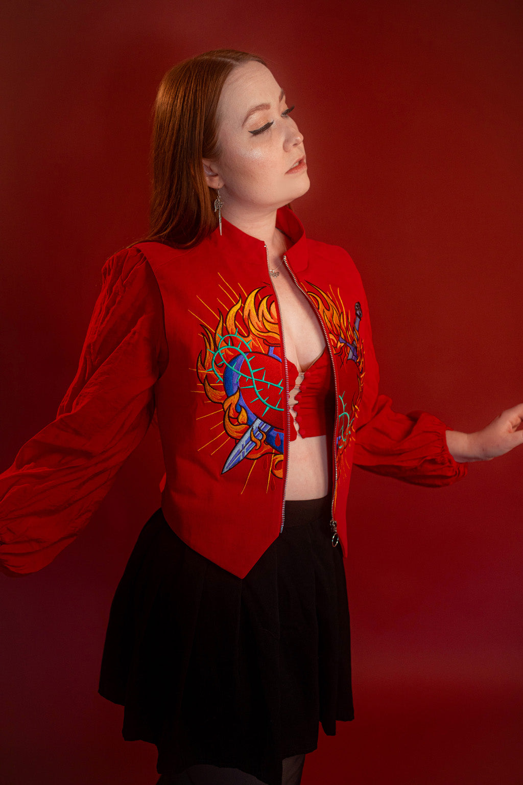 Vibrant red cotton twill vest with zipper front closure and O ring silver zipper. Large, full color orange, yellow, teal, blue, and silver embroidered sacred heart design on chest. Grey and black checkered lining and inner pocket.