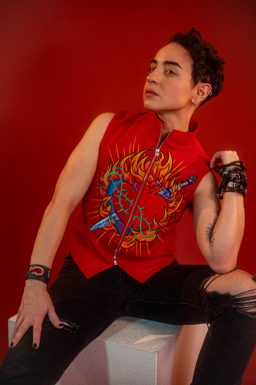 Vibrant red cotton twill vest with zipper front closure and O ring silver zipper. Large, full color orange, yellow, teal, blue, and silver embroidered sacred heart design on chest. Grey and black checkered lining and inner pocket.