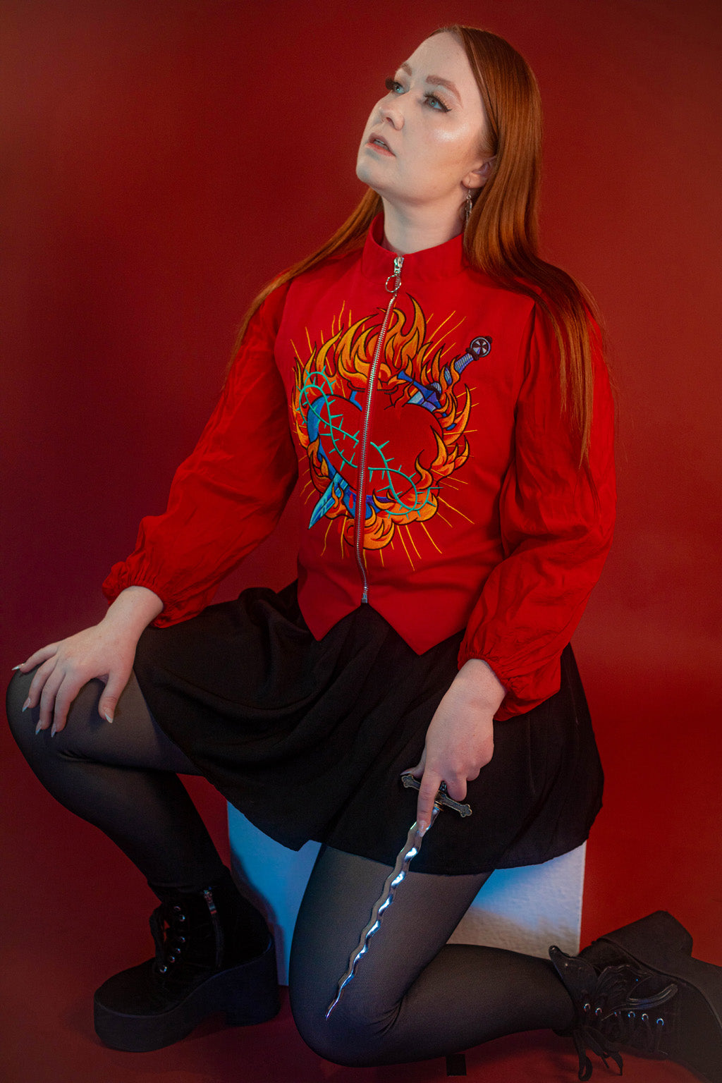 Vibrant red cotton twill vest with zipper front closure and O ring silver zipper. Large, full color orange, yellow, teal, blue, and silver embroidered sacred heart design on chest. Grey and black checkered lining and inner pocket.